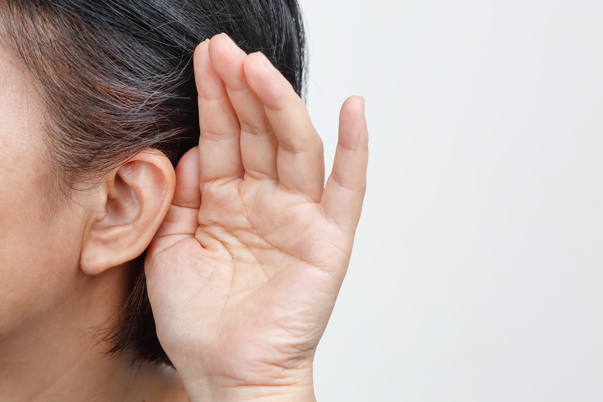Woman cupping hand behind ear, listening intently.
