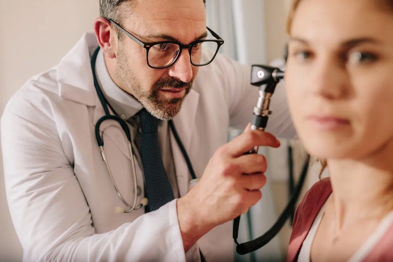 Doctor examining a patient's ear with an otoscope. The doctor is wearing glasses and a stethoscope.