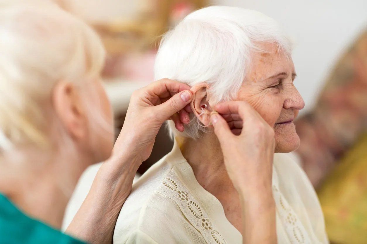 A person putting in a hearing aid for an older woman with white hair; indoors.