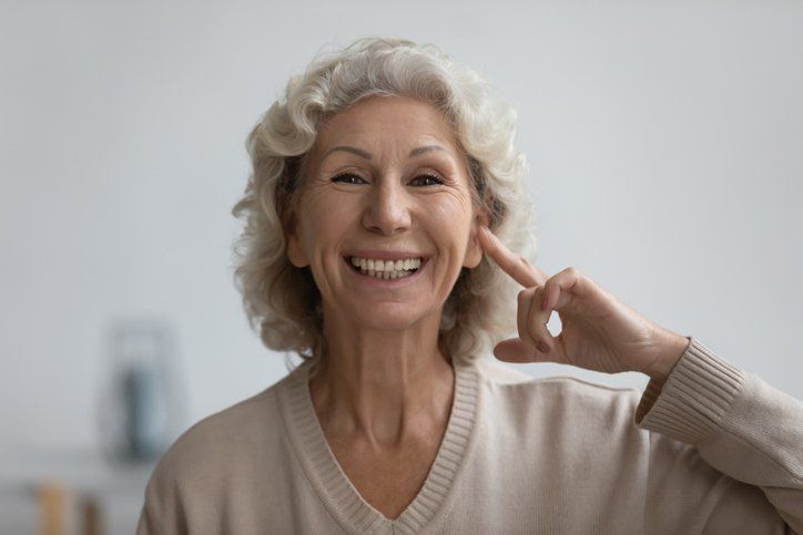 Smiling older woman with white hair points to her ear.