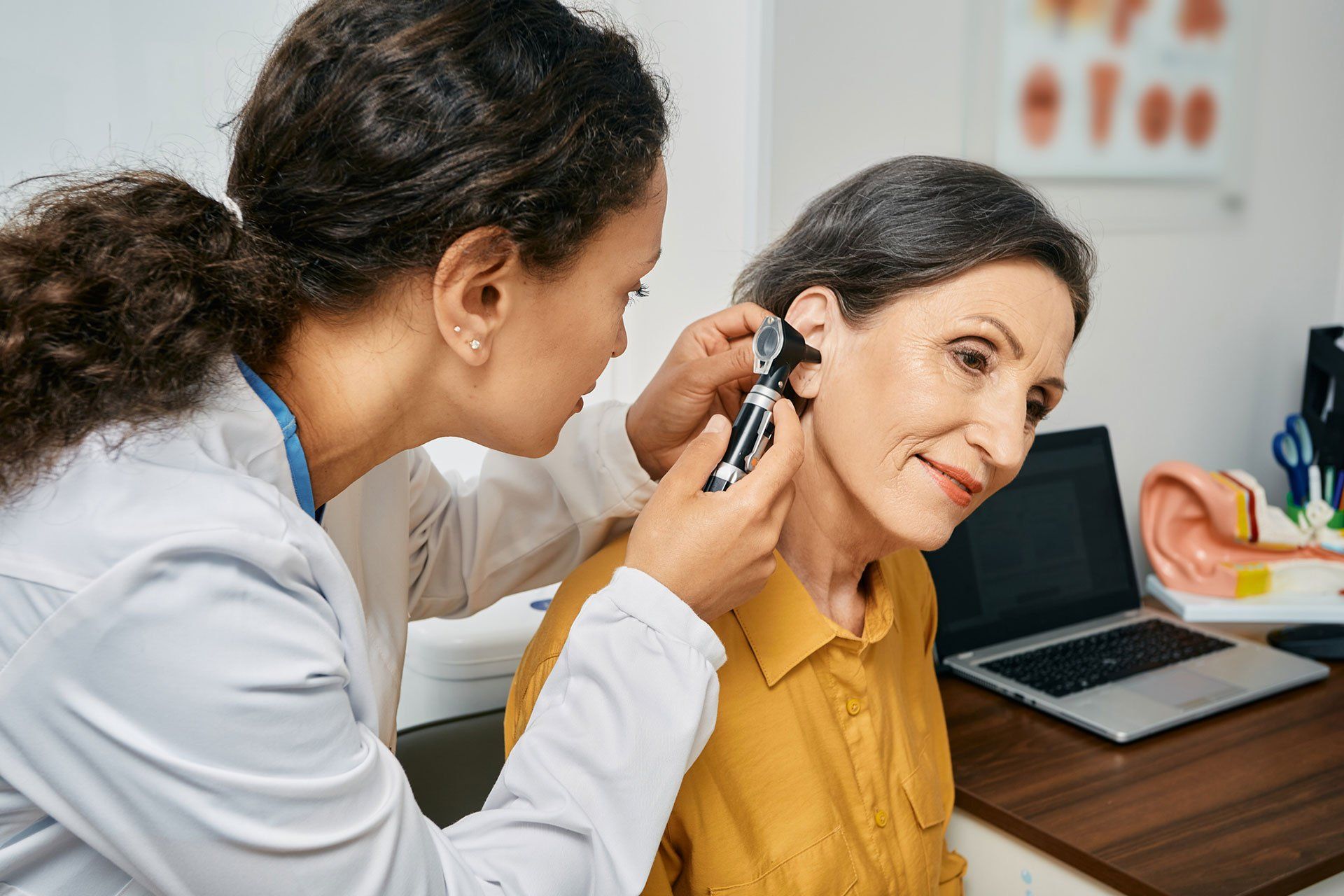 Doctor examining a woman's ear with an otoscope in a medical office.