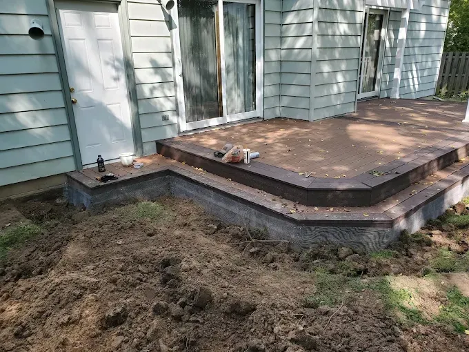 A low retaining wall and steps lead up to a concrete patio. The light blue house has a door and sliding glass door.