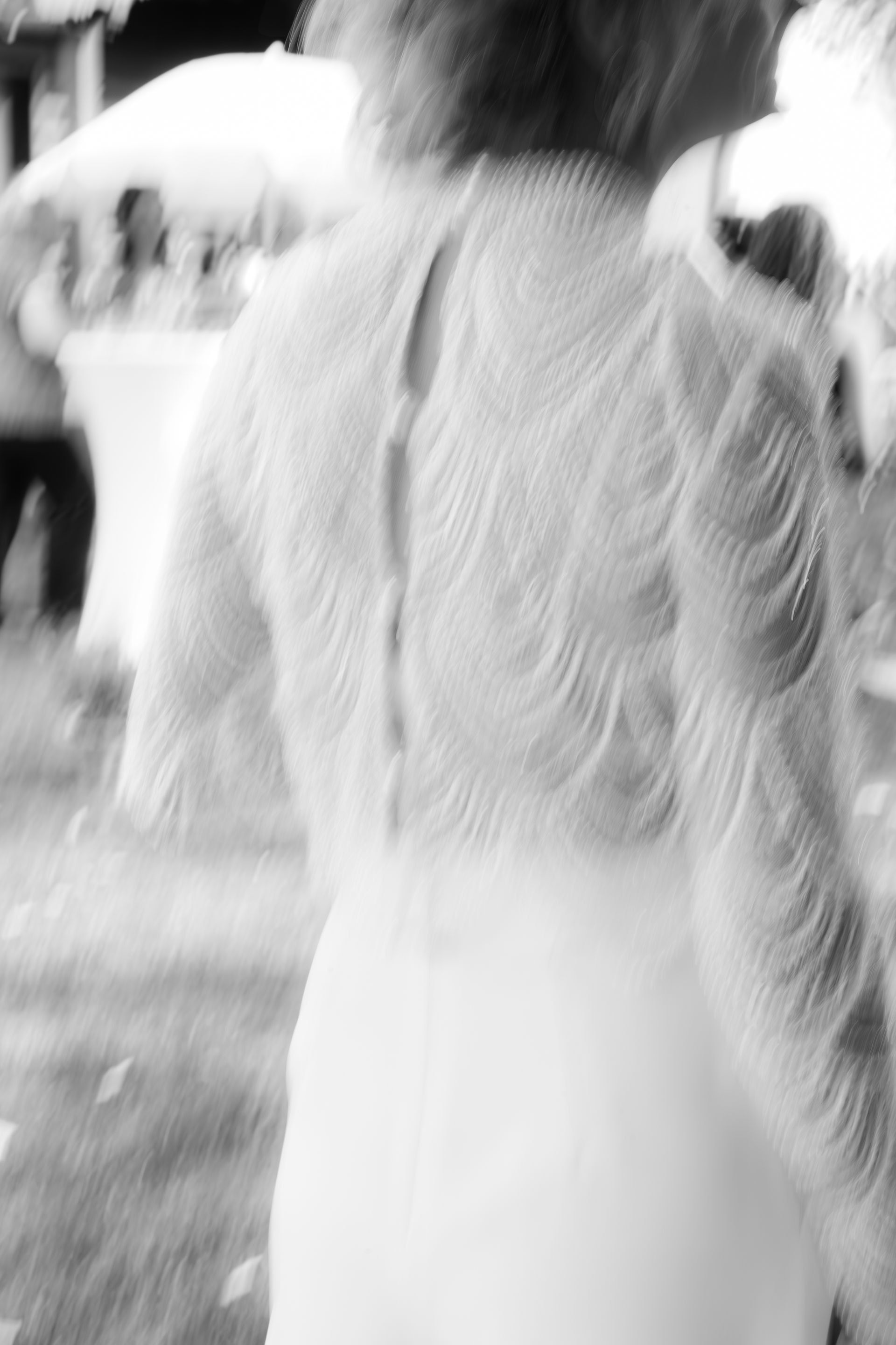 Braut im weißen Kleid, geht weg, aufwendig strukturiertes Rückendesign mit Knöpfen, Außenkulisse.