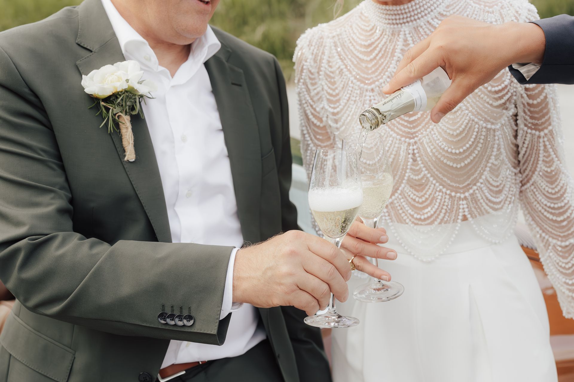 Mann im grünen Anzug und Frau im weißen Kleid, denen bei einer Hochzeit Champagner eingeschenkt wird.