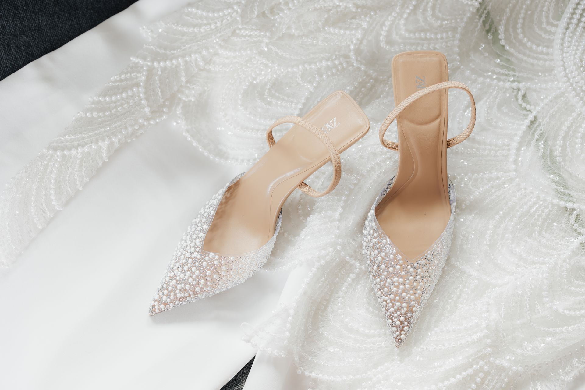 Brautschuhe mit Perlenbesatz auf einem weißen Kleid, auf einer weißen Oberfläche.
