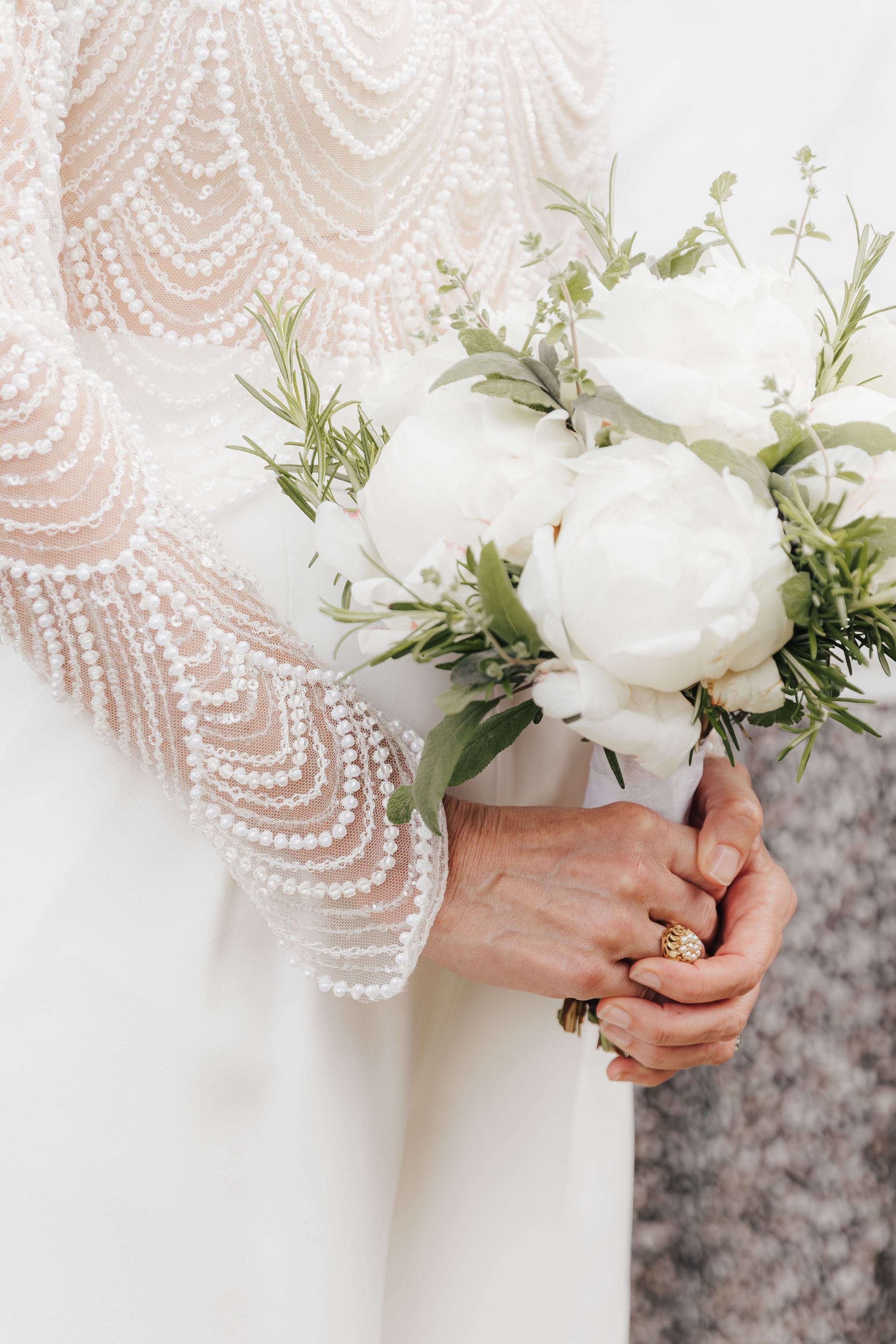 Braut hält weißen Pfingstrosenstrauß und trägt ein weißes Brautkleid mit Perlenärmeln.
