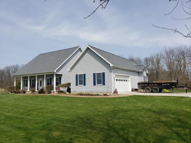A large white house with a gray roof is sitting on top of a lush green field.