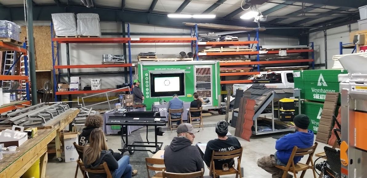 A group of people are sitting in chairs in a warehouse watching a presentation.