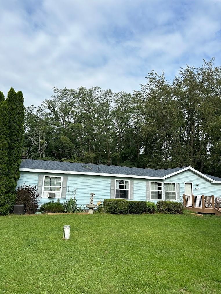 A blue mobile home is sitting in the middle of a lush green field.