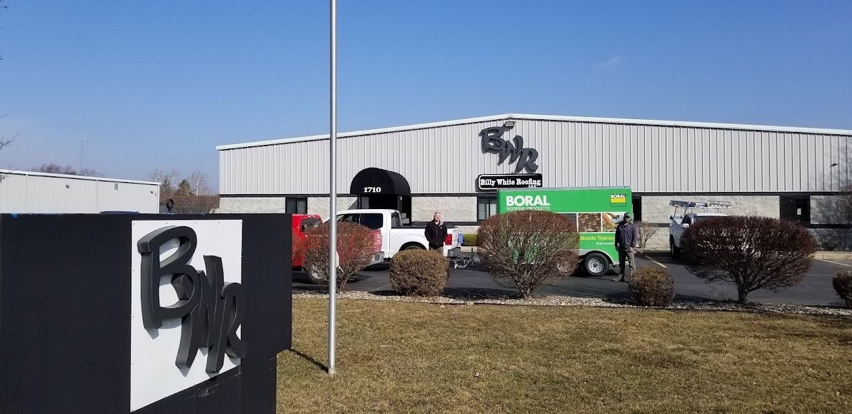 A green food truck is parked in front of a large building.