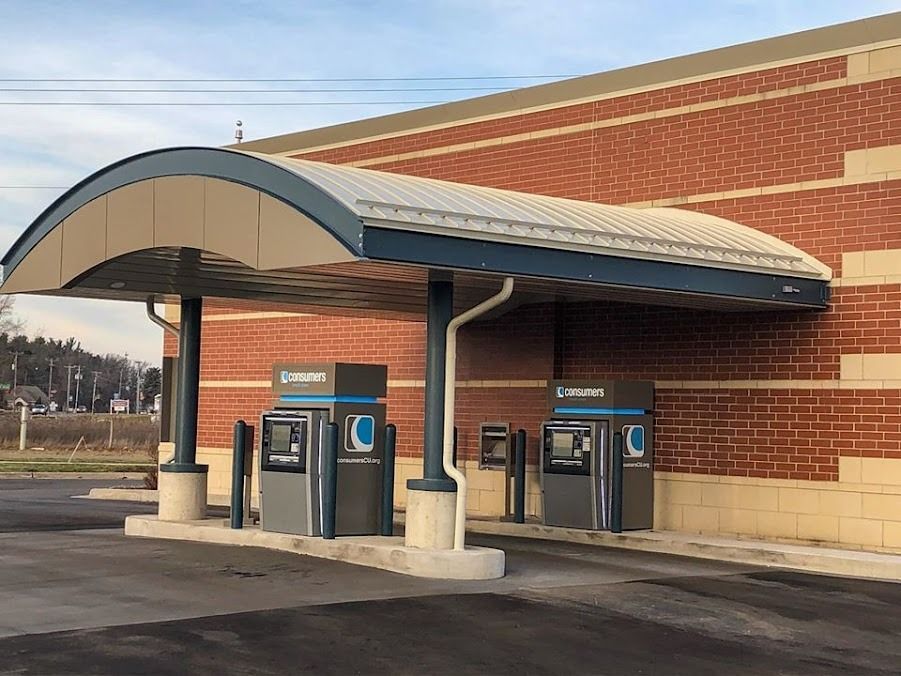 Two atm machines are under a canopy in front of a brick building.