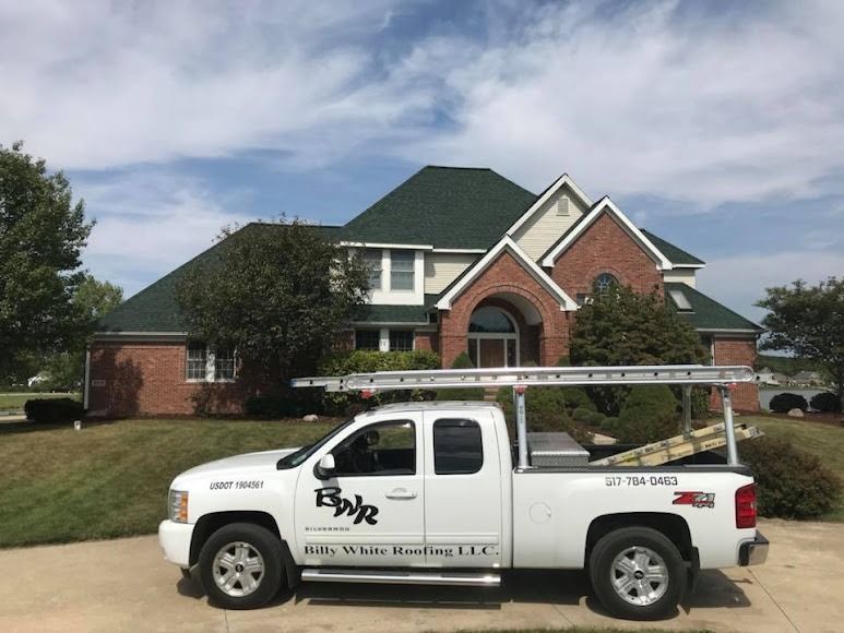 A white truck is parked in front of a house with a green roof