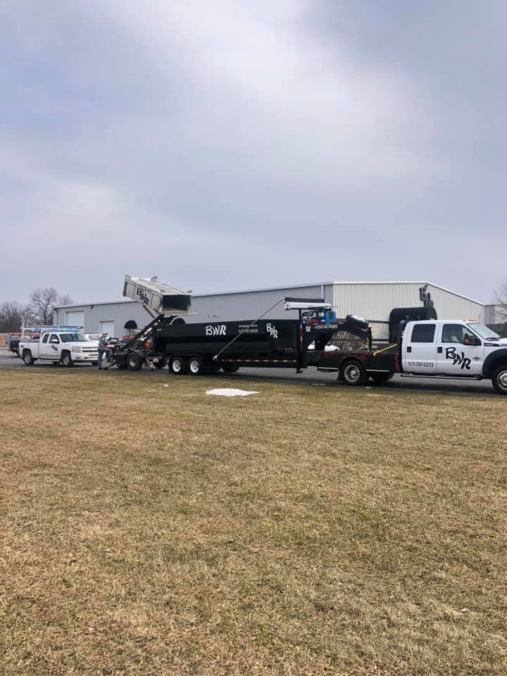 A dump truck is being towed by a truck in a field.