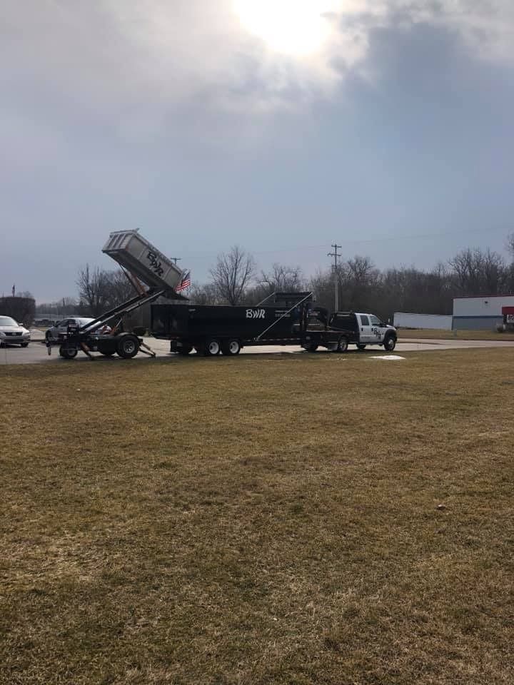 A dump truck is being towed by a trailer in a field.