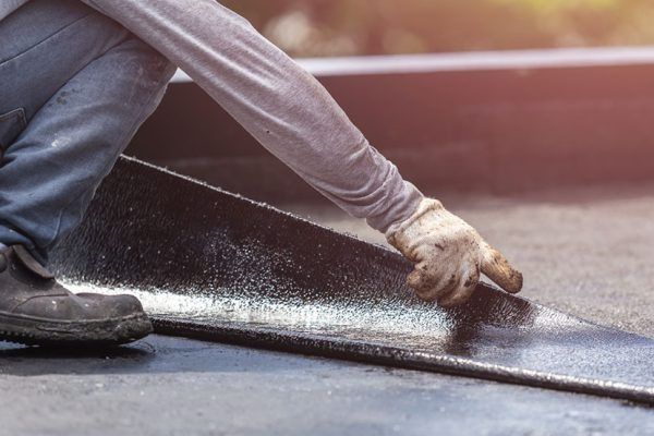 A man is kneeling down and applying a roof coating to a roof.