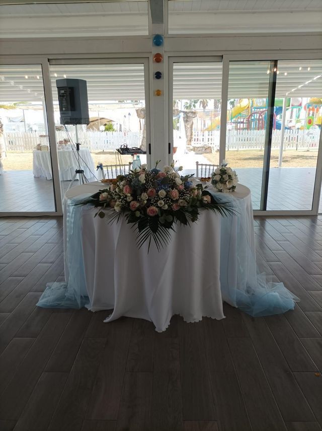 Un tavolo con fiori sopra in una stanza con molte finestre.