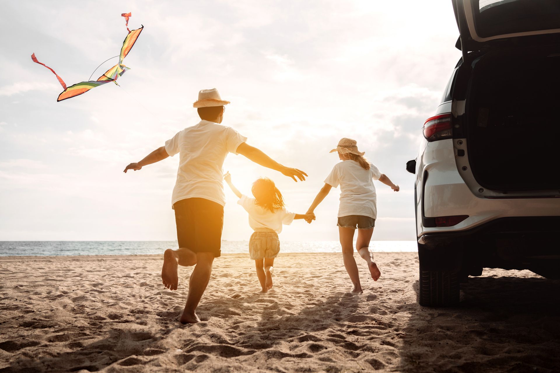 Una famiglia sta facendo volare un aquilone sulla spiaggia accanto a un'auto.