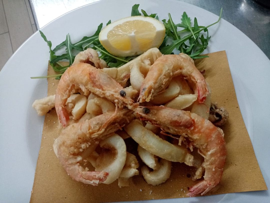 Un piatto bianco condito con gamberi e calamari fritti