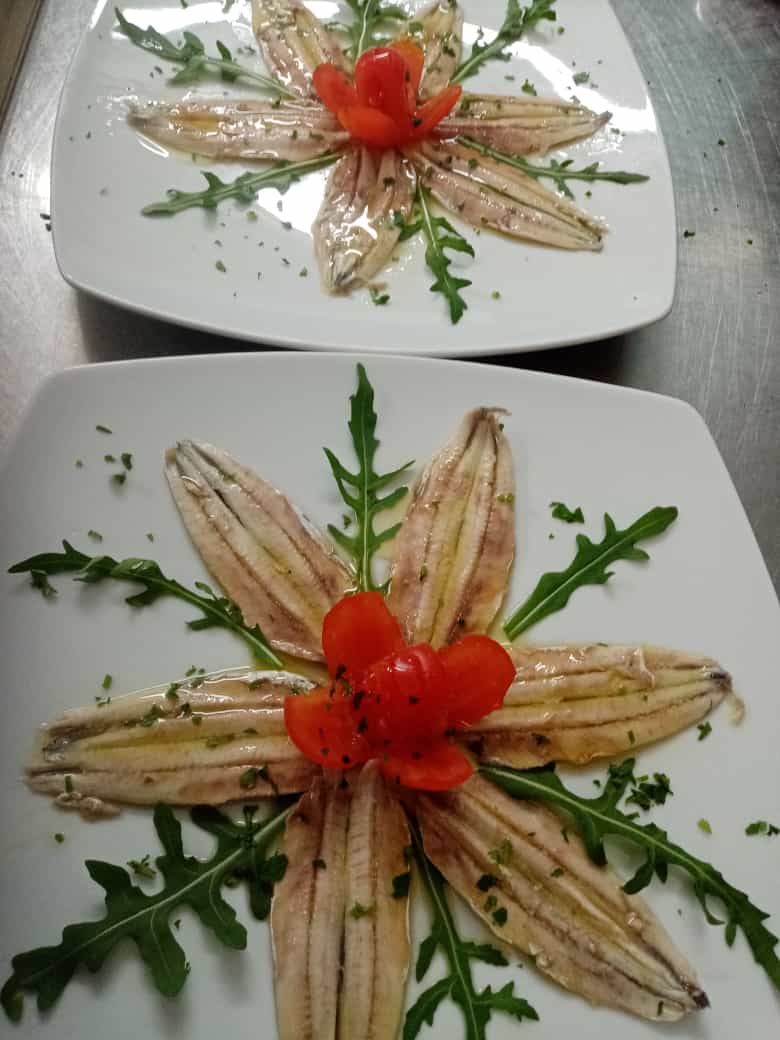 Due piatti di cibo con acciughe e pomodori disposti a forma di fiore
