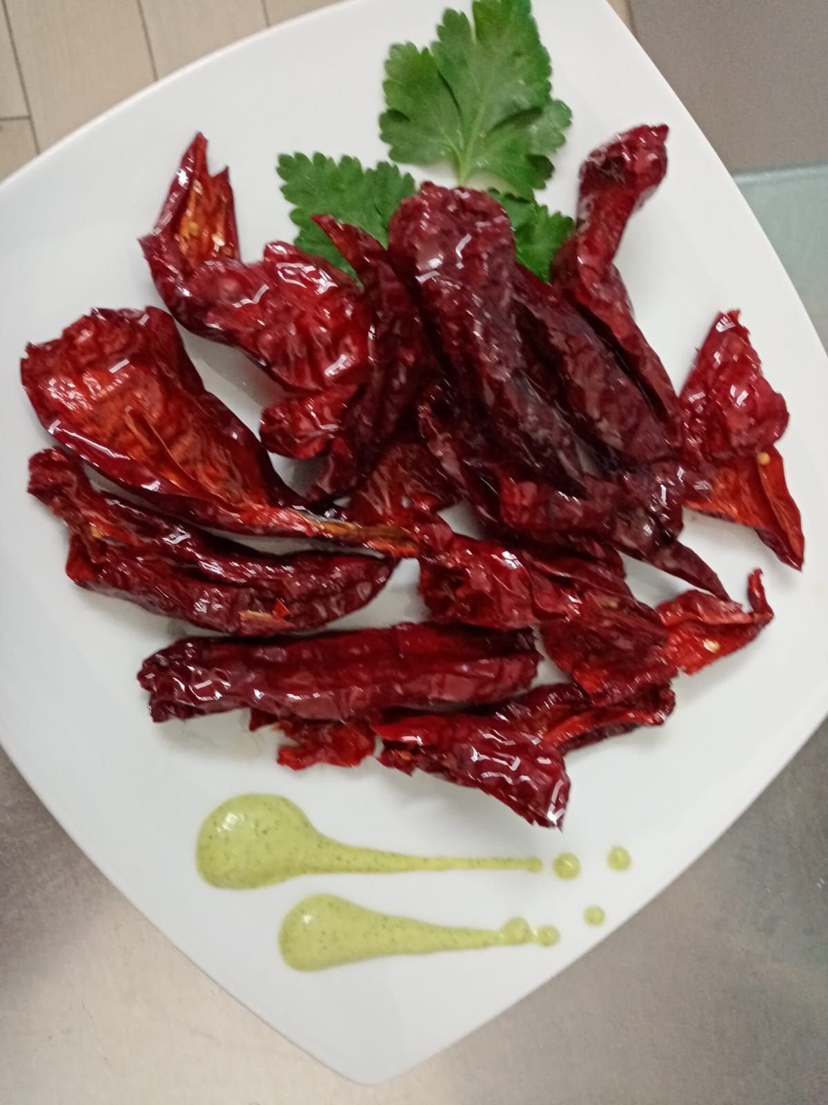 Un piatto bianco condito con peperoni rossi secchi e salsa verde