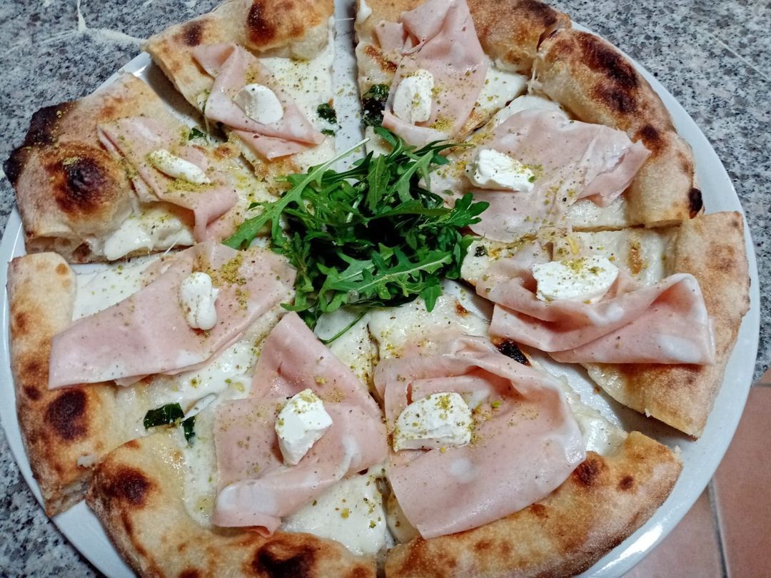 Una pizza con prosciutto e formaggio su un piatto bianco