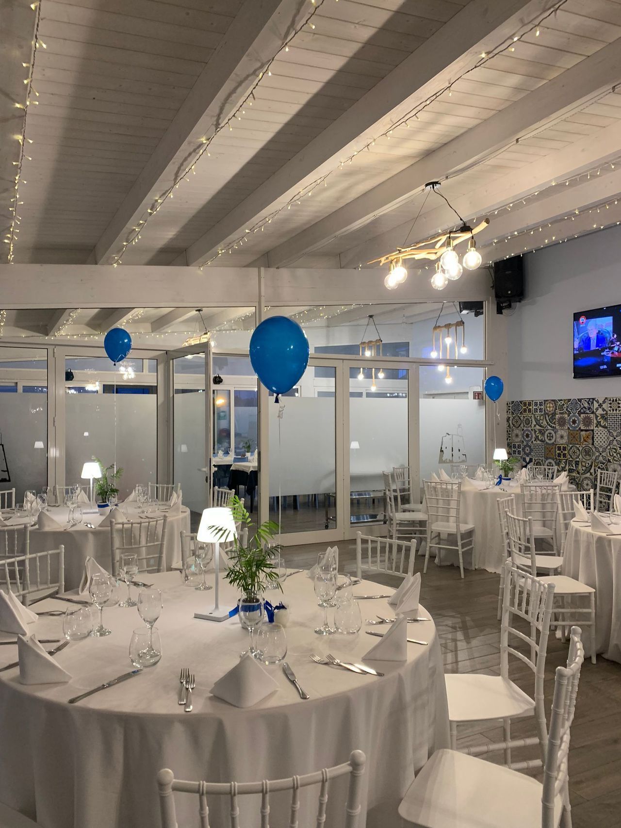 Una grande stanza con tavoli e sedie bianchi e palloncini blu appesi al soffitto