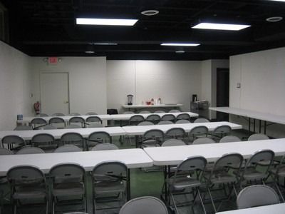 Empty conference room with white tables and chairs, white walls, and a black ceiling.