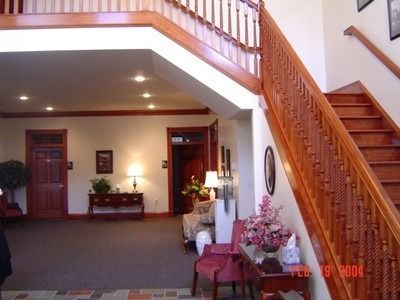 A grand foyer with a wooden staircase, detailed railing, and doors. Includes furniture and decor.