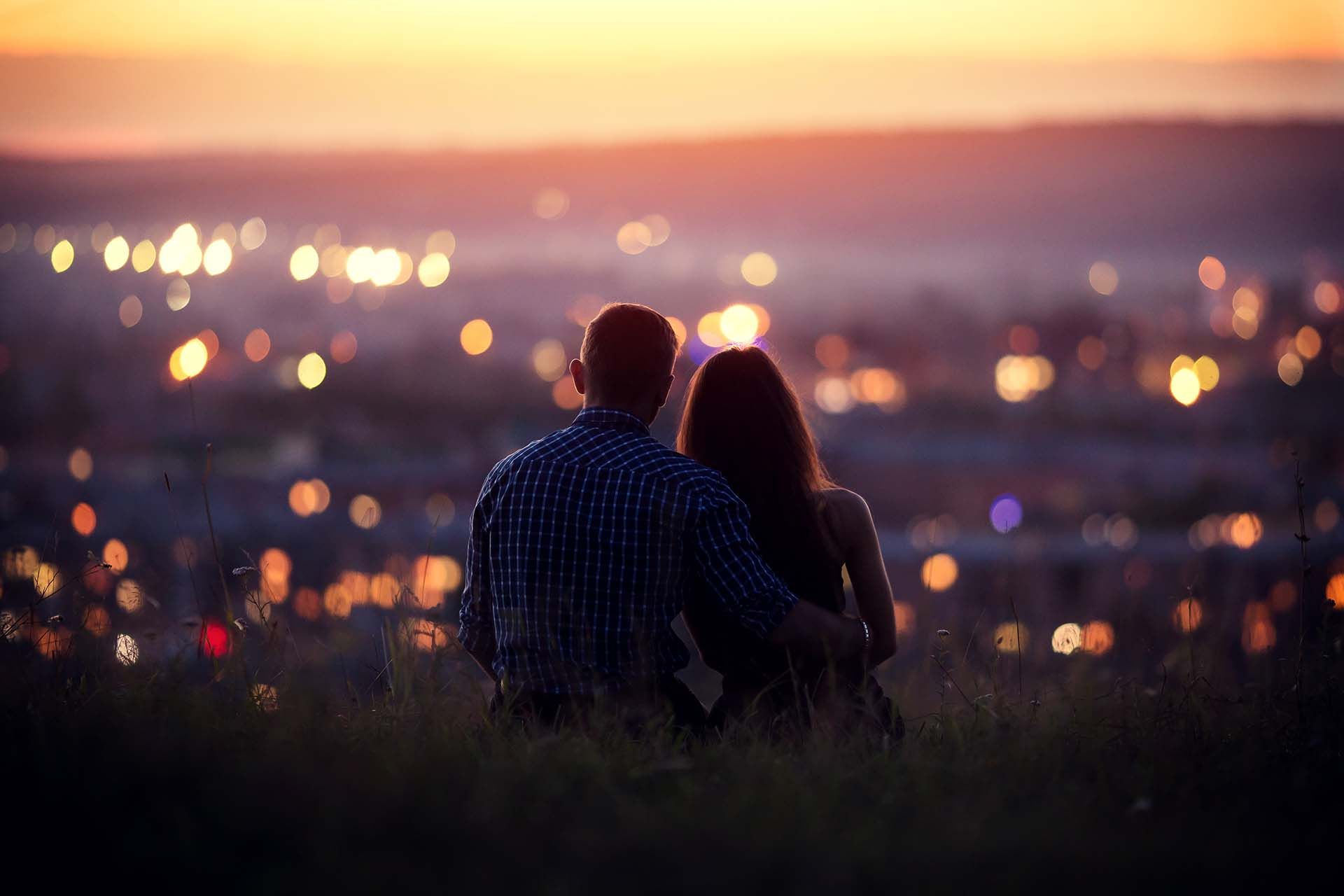Couple embracing, watching city lights at dusk.