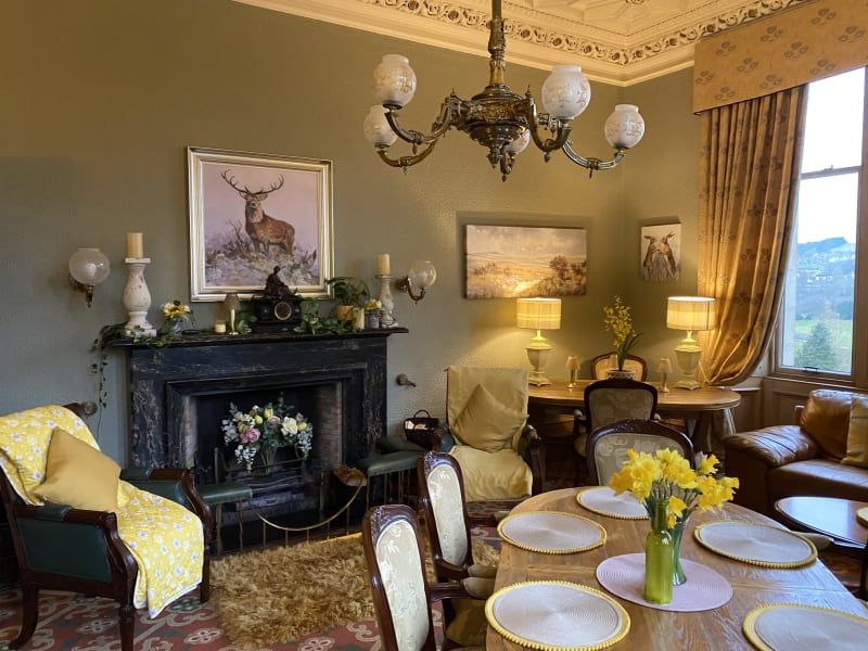 Hotel sitting room, decorated in country-manor style with arm chairs, heavy curtains and patterned carpet