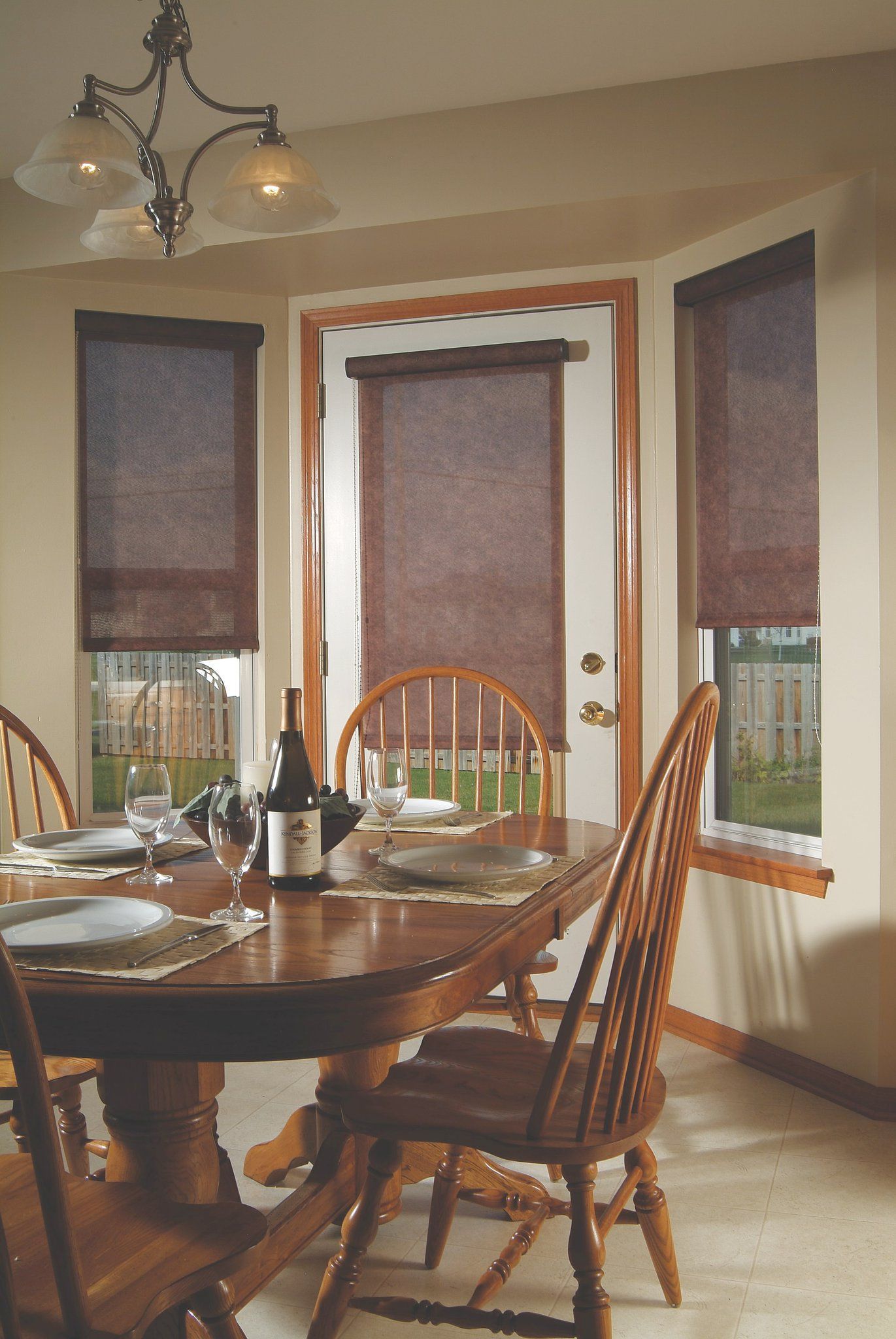 Dining room with round wooden table and chairs, set with plates. Dark brown shades cover windows.
