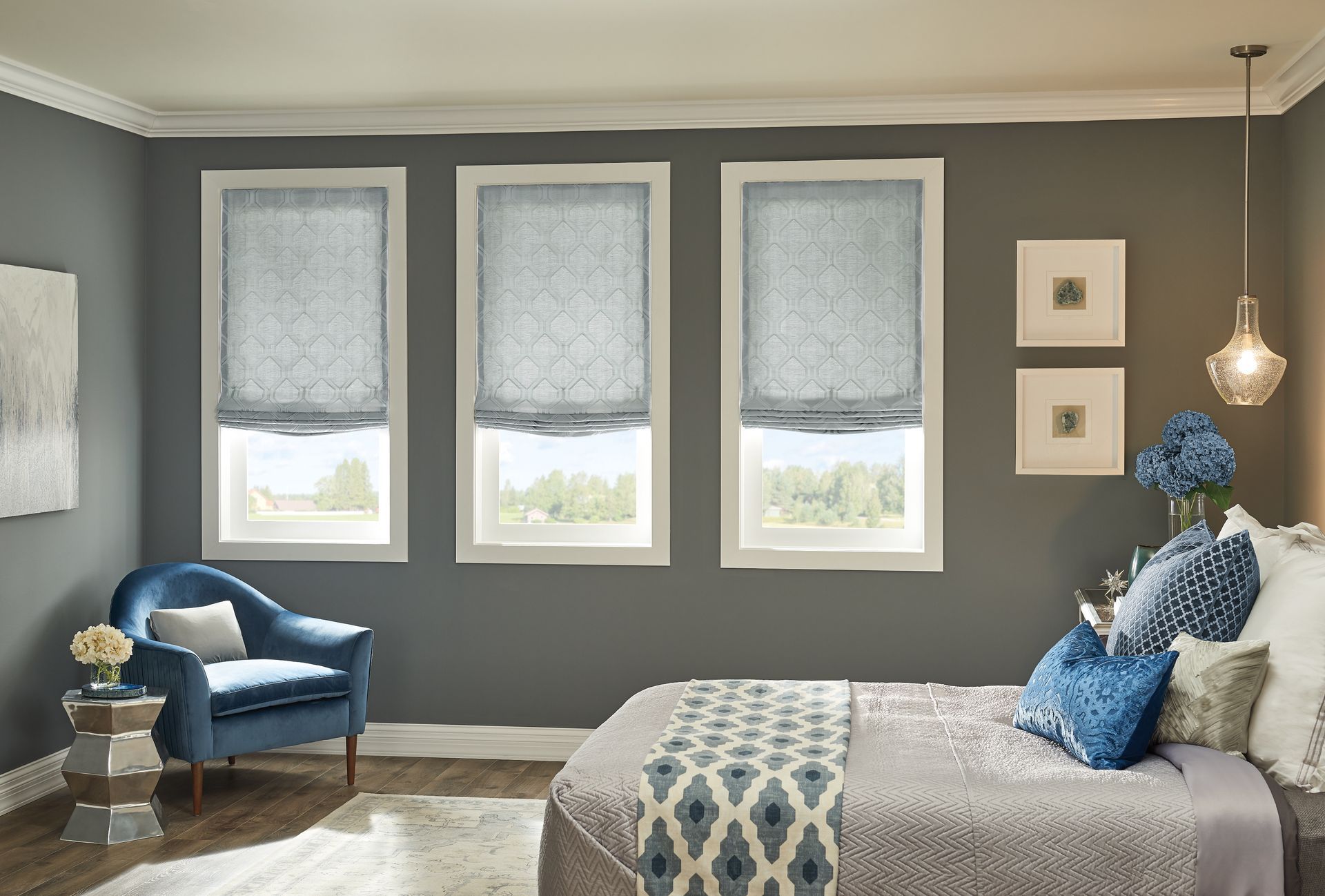 Bedroom with gray walls, three windows with blue shades, blue chair, bed, and decorative accents.