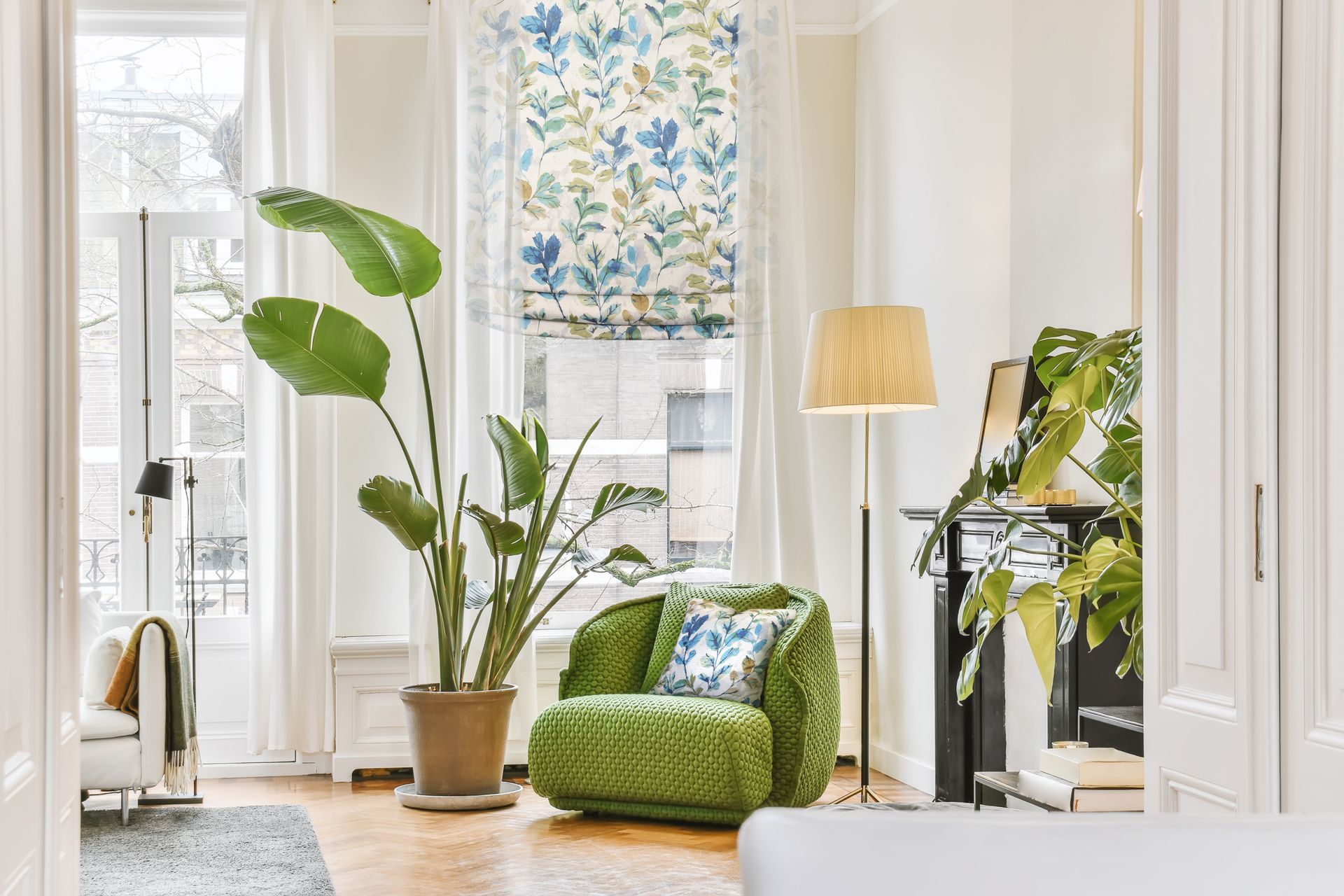 Bright living room with green armchair, large potted plant, and floral window shade.