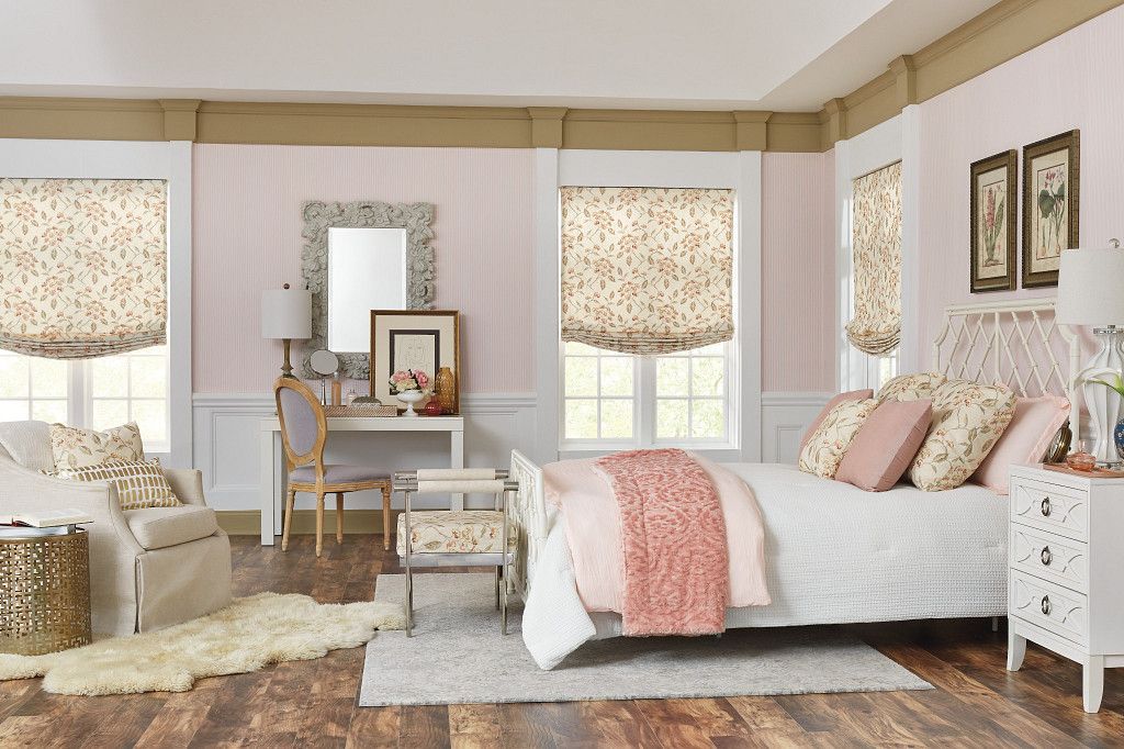 Pink bedroom with white furniture, wood floors, floral window shades, and artwork.