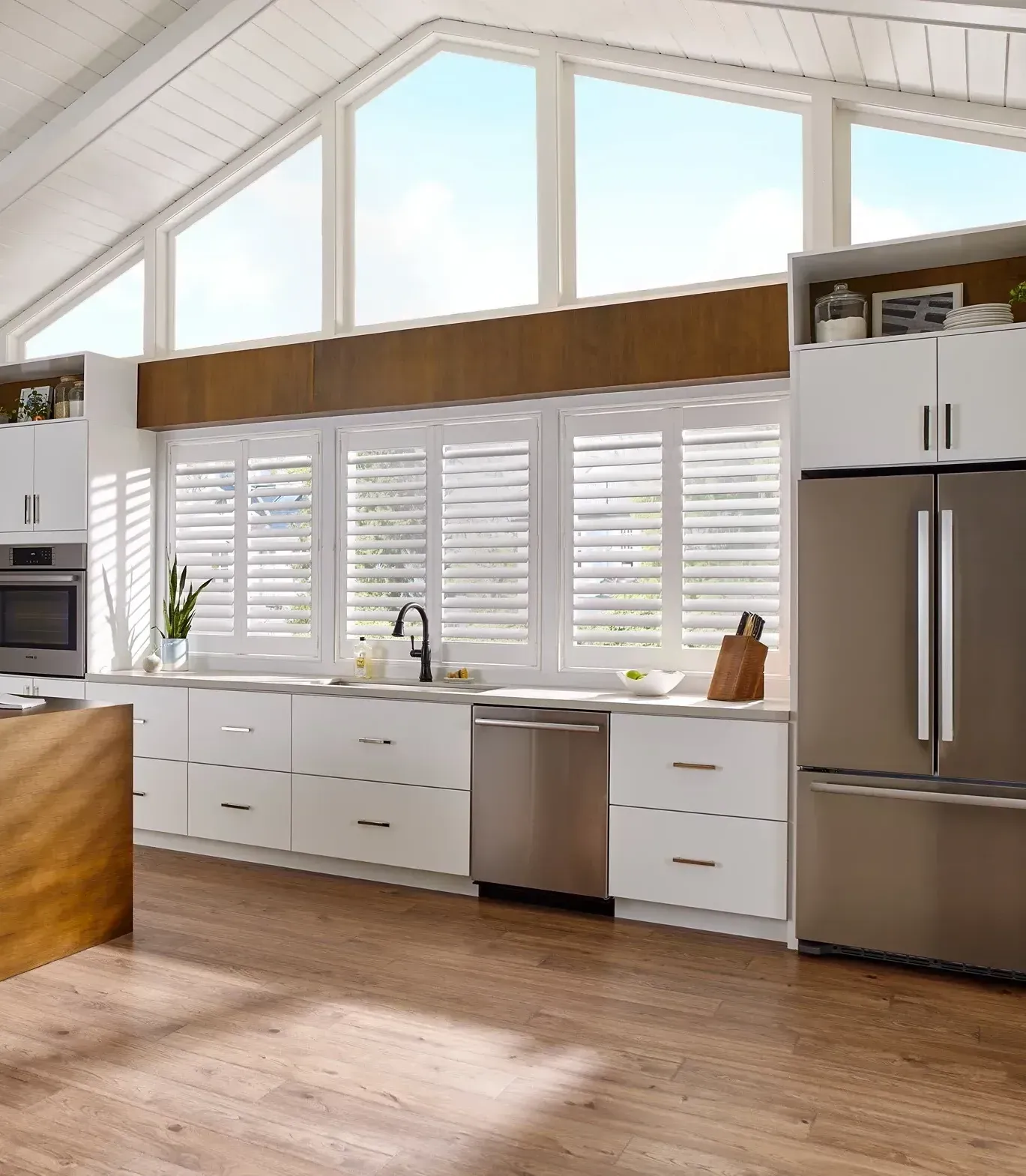 Modern kitchen with white cabinets, stainless steel appliances, and large windows with shutters.