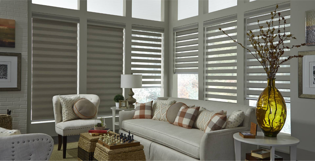 Living room with beige sofa, patterned pillows, neutral blinds, and tall glass vase.