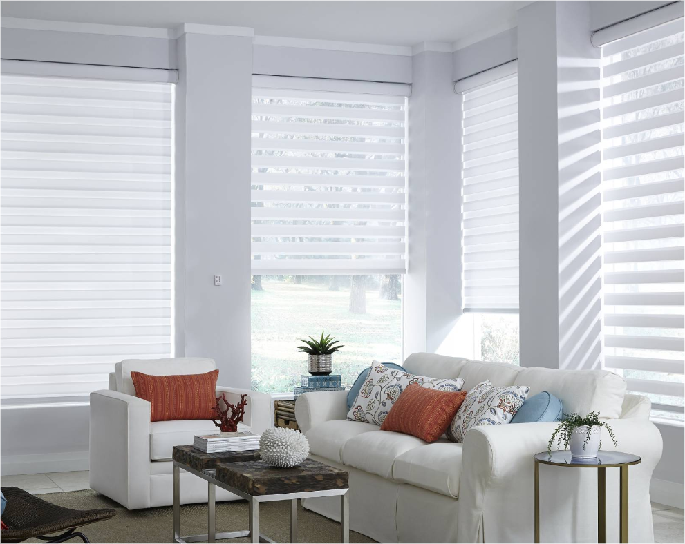 Living room with white blinds, sofa, chairs, and colorful pillows.