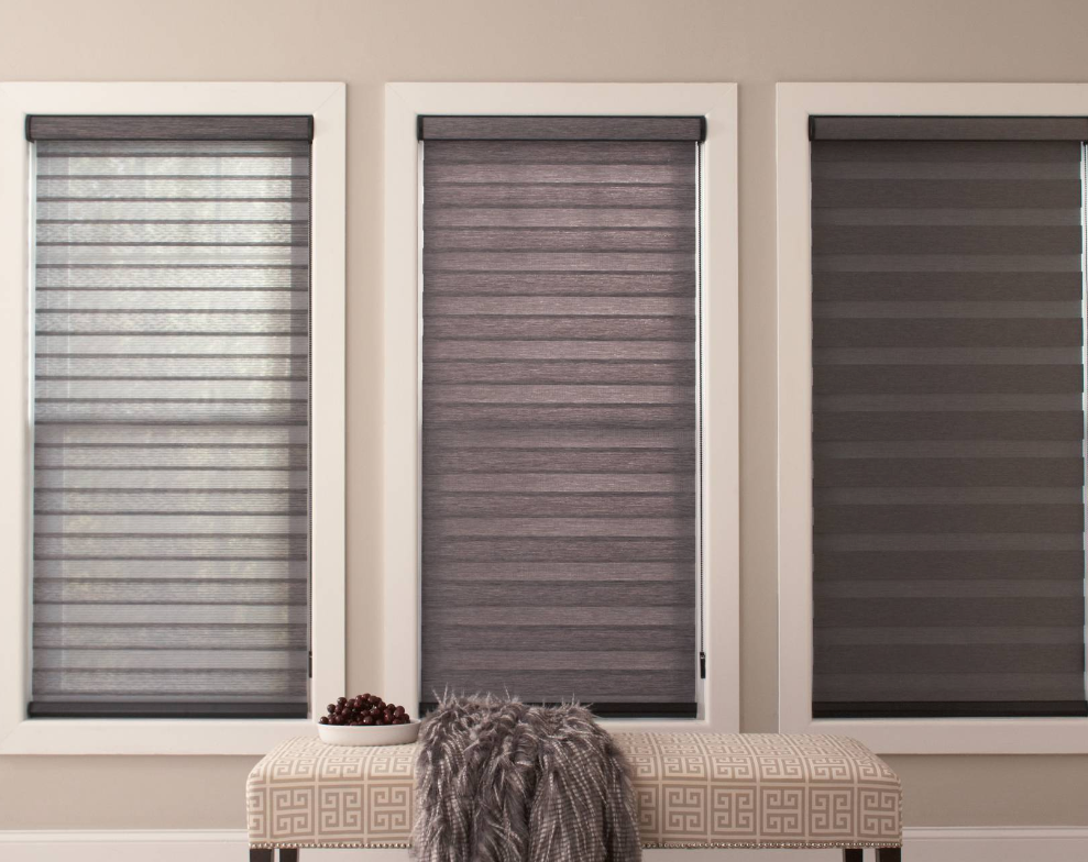 Three windows with shades in varying shades of grey, above a bench with a fur throw.