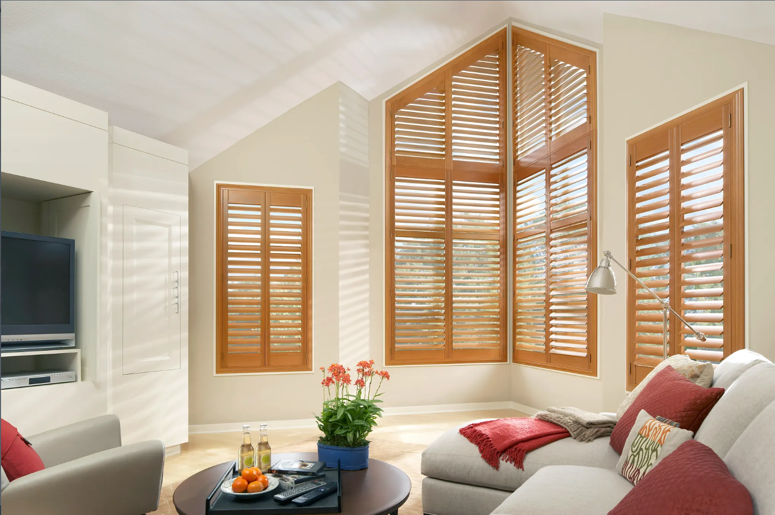 Living room with wooden shutters, white couch, round table, and a TV.