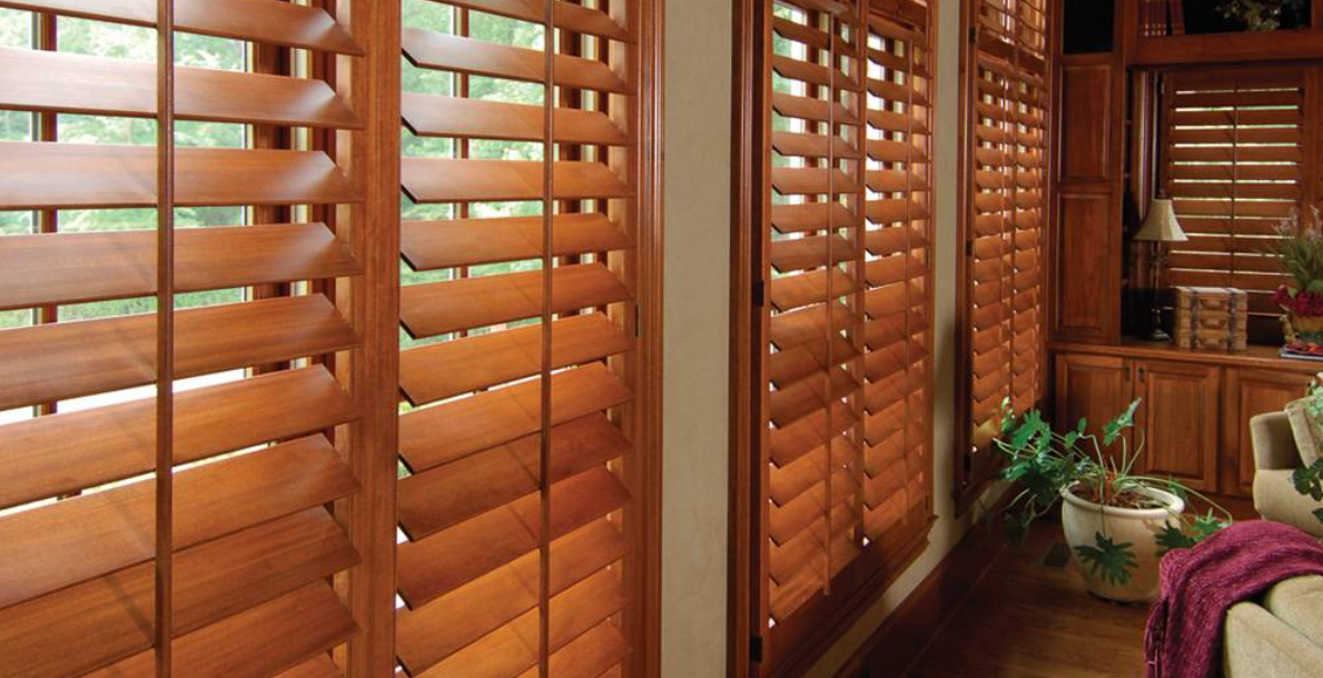 Wooden shutters on a window, with slats open, filtering light. Interior shot of a room.