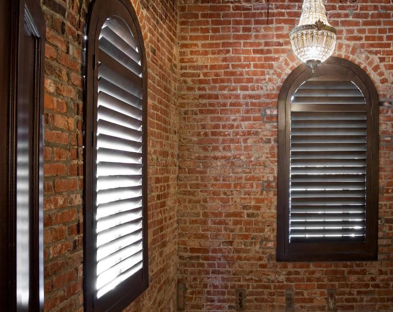Brick walls with arched windows, dark wood shutters, and a chandelier.