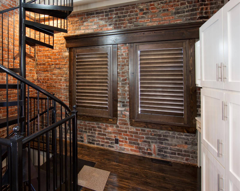 Spiral staircase and shuttered windows on a brick wall, next to white cabinets.