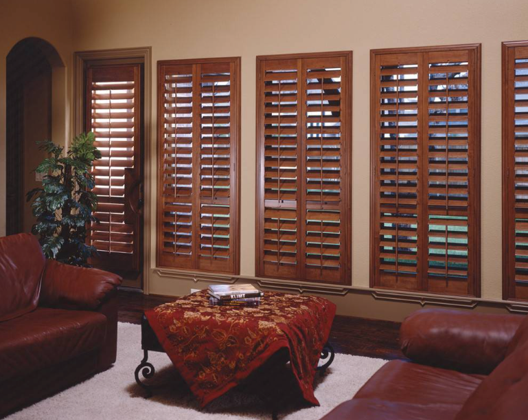 Living room with wood shutters, brown leather furniture, and patterned coffee table.