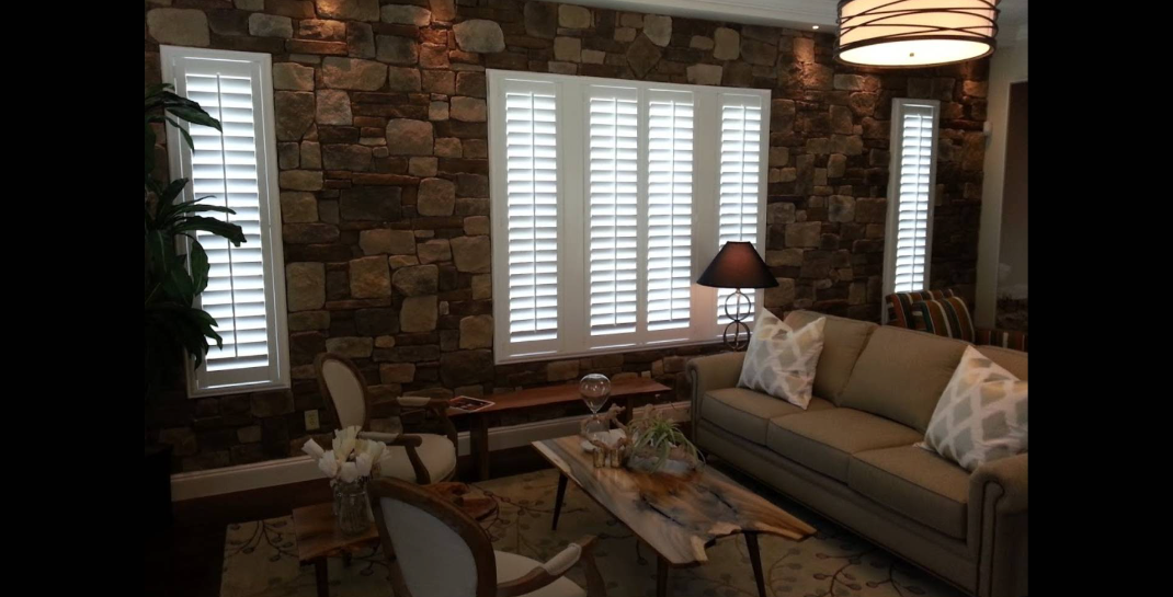 Living room with stone wall, white shutters, beige sofa, and natural light.