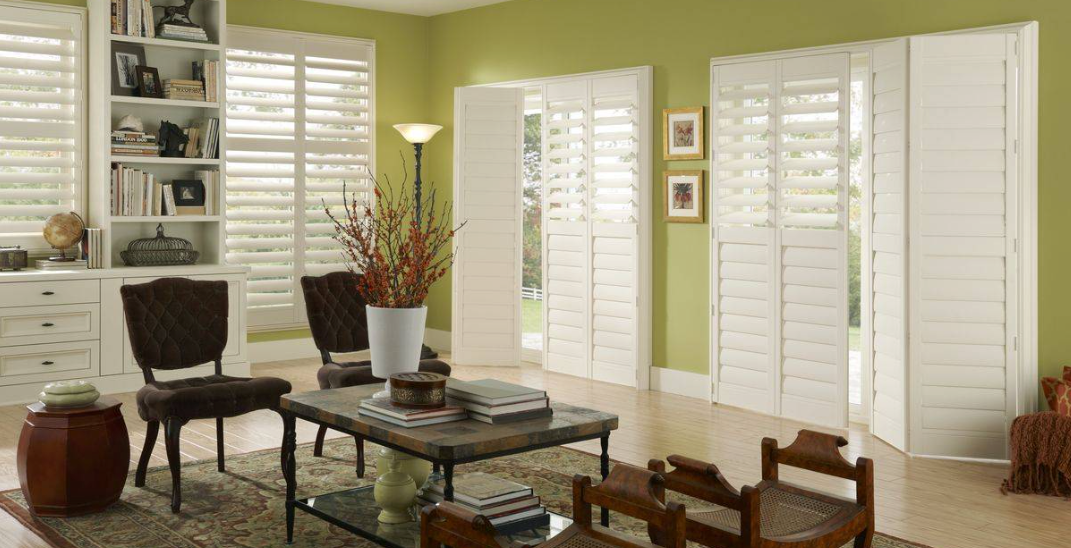 Living room with white shutters, green walls, and wood furniture.