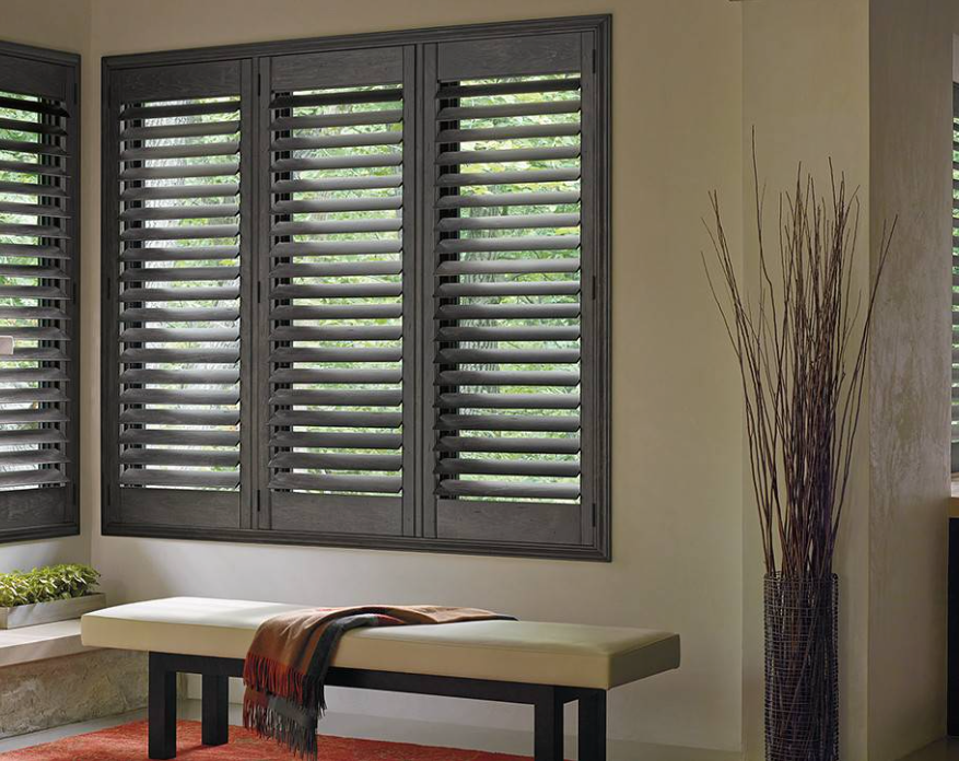 Dark wooden shutters on windows, beige bench with a blanket, tall decorative vase.
