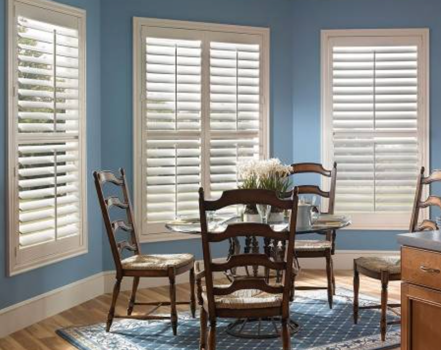 Dining room with blue walls, white shutters, round table, and wooden chairs.