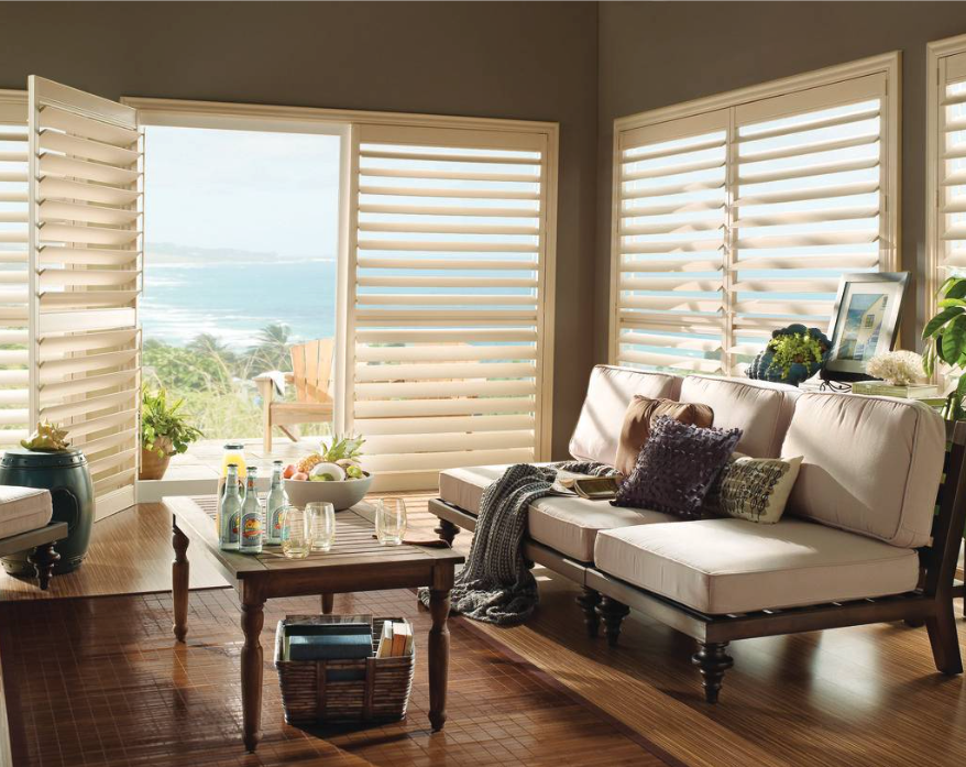 Living room with beige shutters, wood floors, and a view of the ocean.