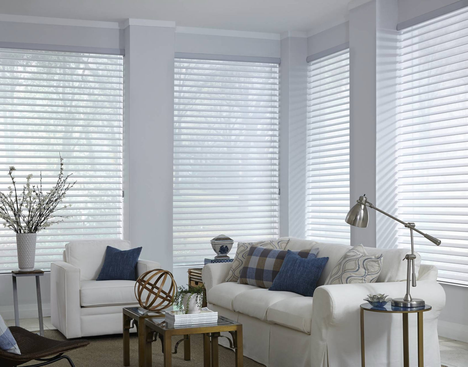 Living room with white furniture, blue pillows, and blinds, natural light.