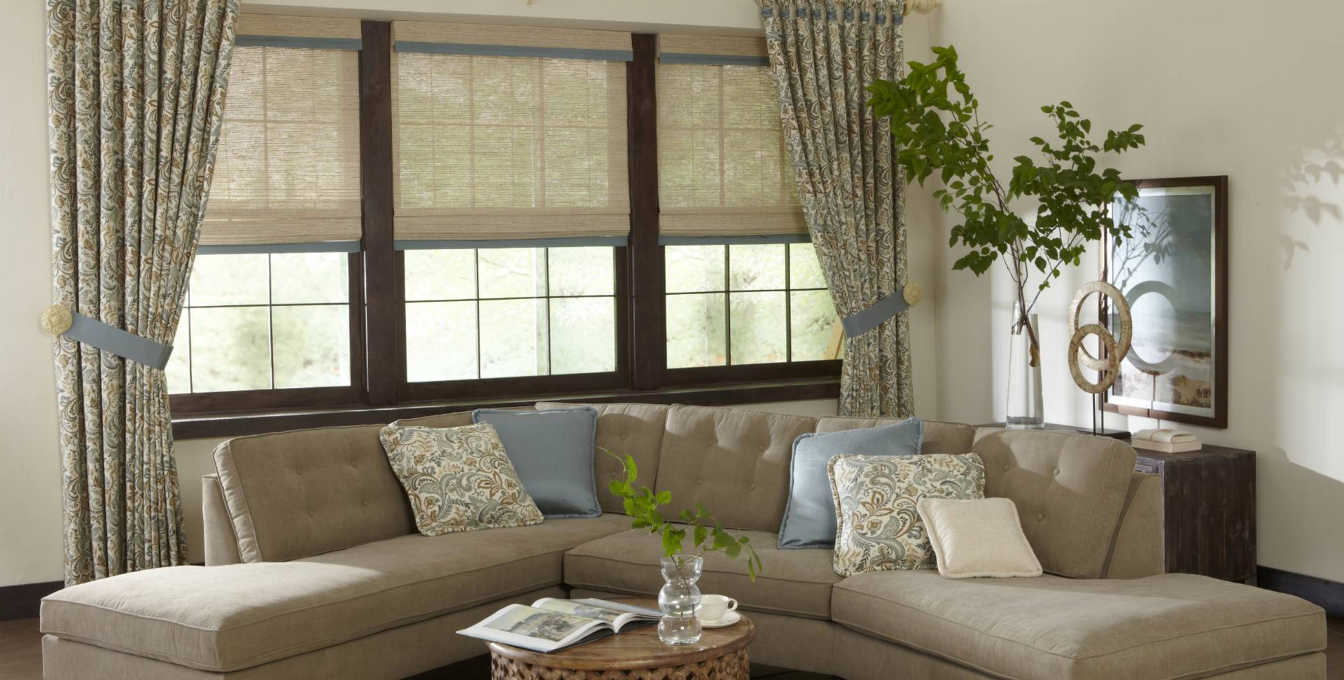 Living room with beige sectional sofa, window with blinds and patterned curtains.